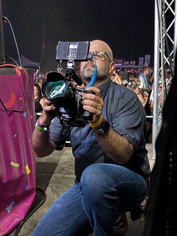 Videograf Bodo Kern filmt kniend am Bühnenrand vor Festivalpublikum – Eventvideos Braunschweig Wolfsburg